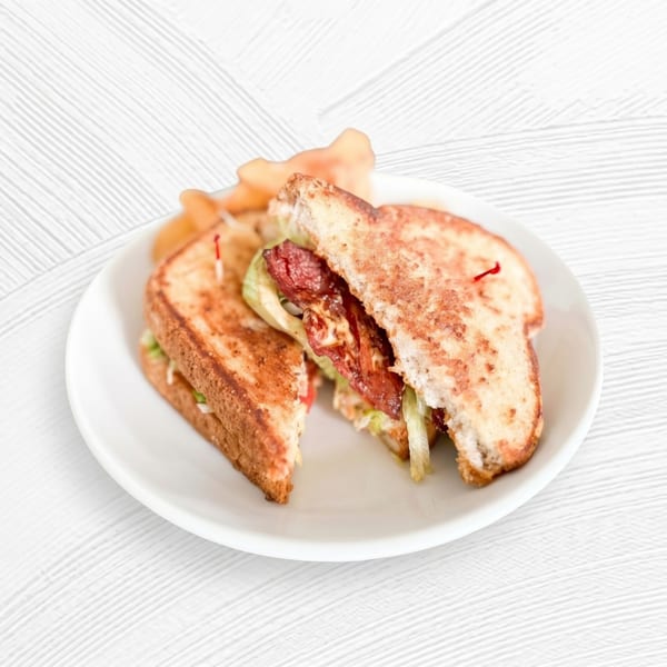 Grilled sandwich halves with bacon, lettuce, and sauce, served with chips on a white plate.